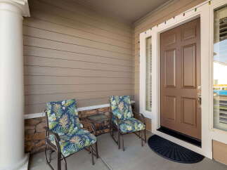 Welcome guests to your charming home with this inviting front porch, featuring two comfortable chairs with tropical-themed cushions and a convenient side table.