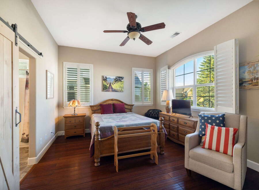 This charming bedroom features a rustic barn door, a comfortable queen-size bed with a patterned quilt, and a wooden quilt rack.