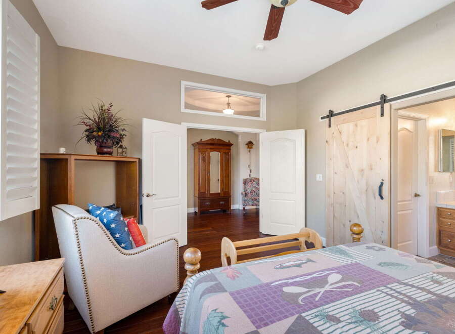 Experience comfort and style in this inviting bedroom, featuring a plush armchair with patriotic pillows and a cozy bed adorned with a nature-themed quilt.