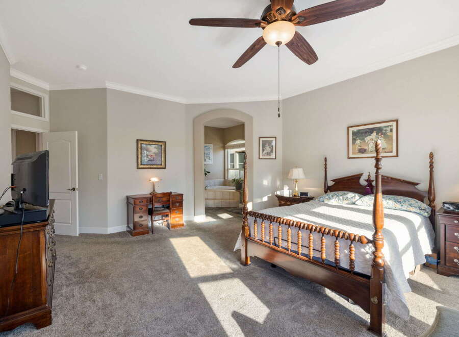 Experience luxurious living in this spacious master suite, featuring a grand four-poster bed and elegant wooden furniture.