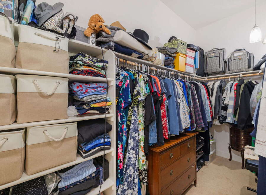 Discover ample storage solutions in this spacious walk-in closet, featuring a variety of shelving, fabric bins, and a charming antique dresser.