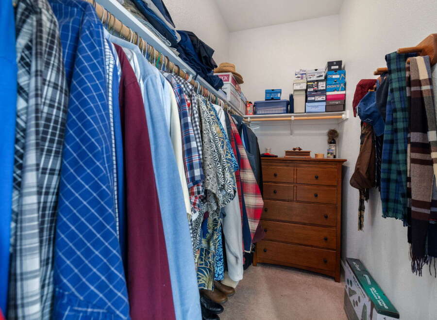 Discover ample storage in this spacious walk-in closet, featuring a well-organized hanging rod system and a charming wooden dresser.