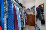 Discover ample storage in this spacious walk-in closet, featuring a well-organized hanging rod system and a charming wooden dresser.