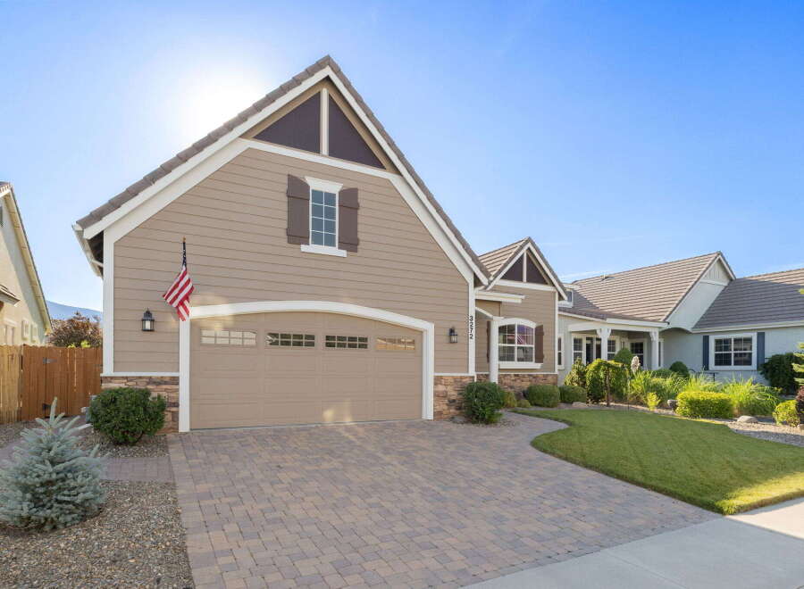 This charming home features a welcoming facade with a tan siding, stone accents, and a classic American flag proudly displayed.
