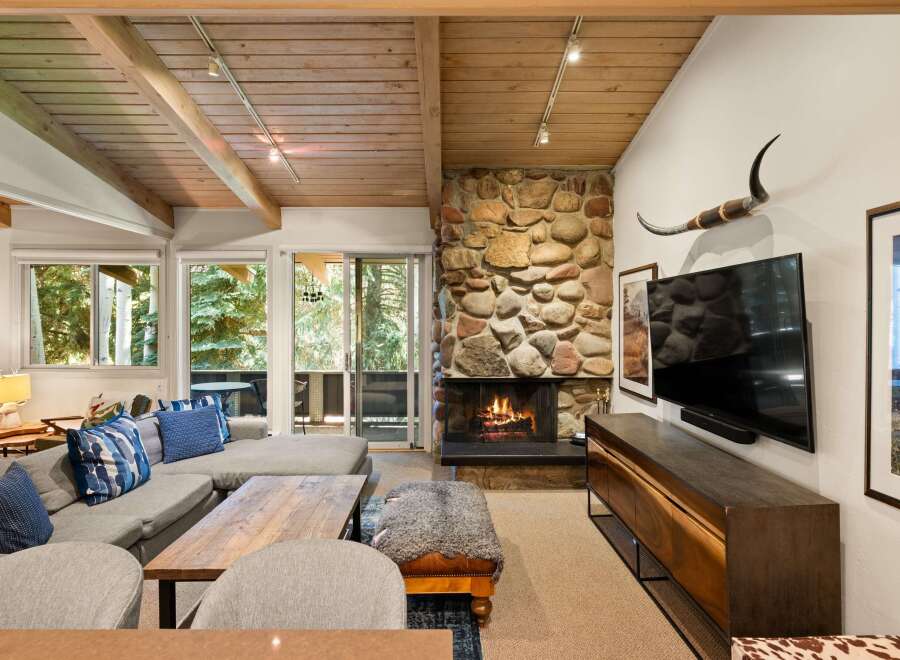 Experience cozy mountain living in this inviting living room, featuring a striking stone fireplace and a vaulted wood-beamed ceiling.