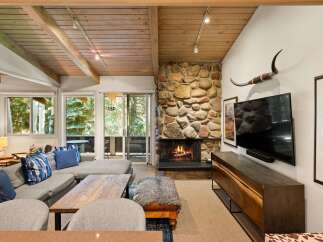 Experience cozy mountain living in this inviting living room, featuring a striking stone fireplace and a vaulted wood-beamed ceiling.