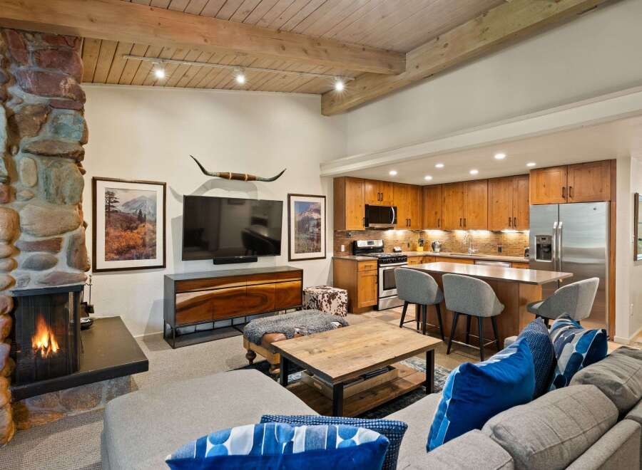 Experience rustic charm and modern convenience in this open-concept living space, featuring a striking stone fireplace and a fully equipped kitchen with warm wood cabinetry.