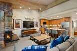 Experience rustic charm and modern convenience in this open-concept living space, featuring a striking stone fireplace and a fully equipped kitchen with warm wood cabinetry.