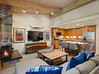 Experience rustic charm and modern convenience in this open-concept living space, featuring a striking stone fireplace and a fully equipped kitchen with warm wood cabinetry.