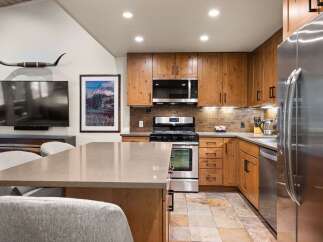 This modern kitchen boasts beautiful natural wood cabinetry complemented by a sleek stainless steel appliance suite, including a microwave, oven, and refrigerator.