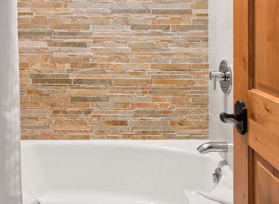Experience luxury in this bathroom featuring a stunning stacked stone accent wall behind a pristine white bathtub.