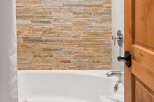 Experience luxury in this bathroom featuring a stunning stacked stone accent wall behind a pristine white bathtub.