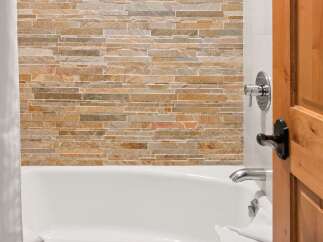 Experience luxury in this bathroom featuring a stunning stacked stone accent wall behind a pristine white bathtub.