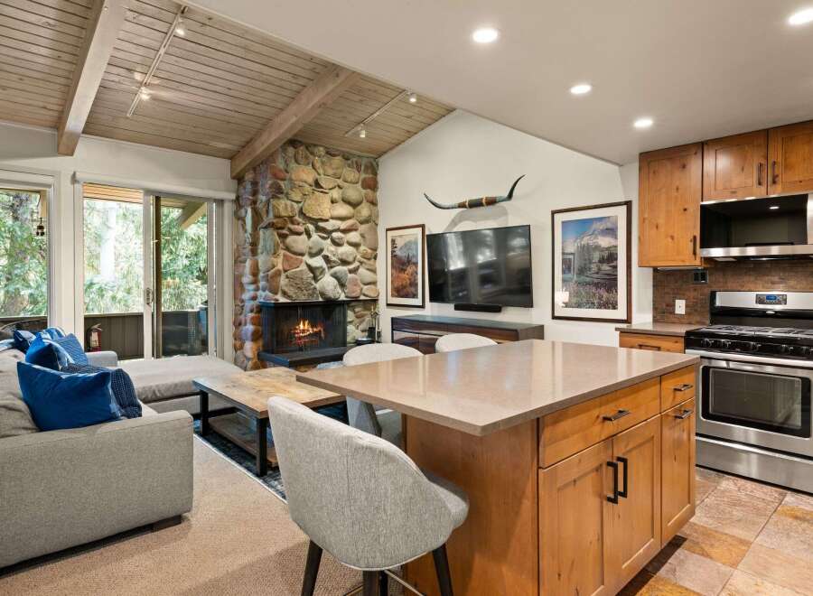 Experience rustic charm in this open-concept living space, featuring a striking stone fireplace and a vaulted wood-beamed ceiling.