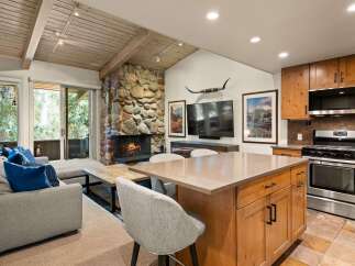 Experience rustic charm in this open-concept living space, featuring a striking stone fireplace and a vaulted wood-beamed ceiling.