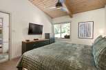 This inviting bedroom features a vaulted wood-paneled ceiling with a modern ceiling fan and track lighting, creating a warm and airy ambiance.