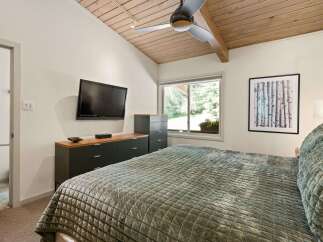 This inviting bedroom features a vaulted wood-paneled ceiling with a modern ceiling fan and track lighting, creating a warm and airy ambiance.