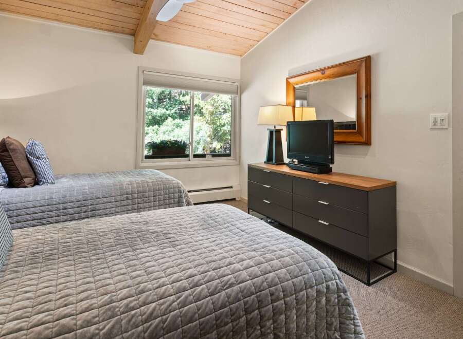 This charming bedroom features two comfortable beds with quilted grey comforters and decorative pillows, perfect for a restful night's sleep.