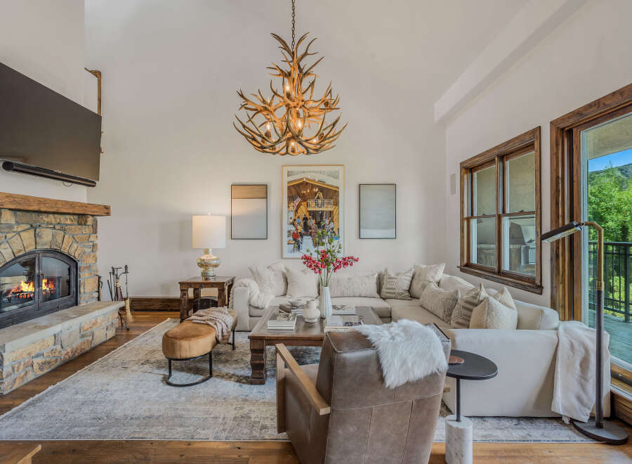 Experience rustic elegance in this spacious living room, featuring a grand stone fireplace and a unique antler chandelier.