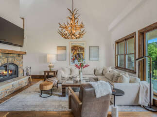 Experience rustic elegance in this spacious living room, featuring a grand stone fireplace and a unique antler chandelier.