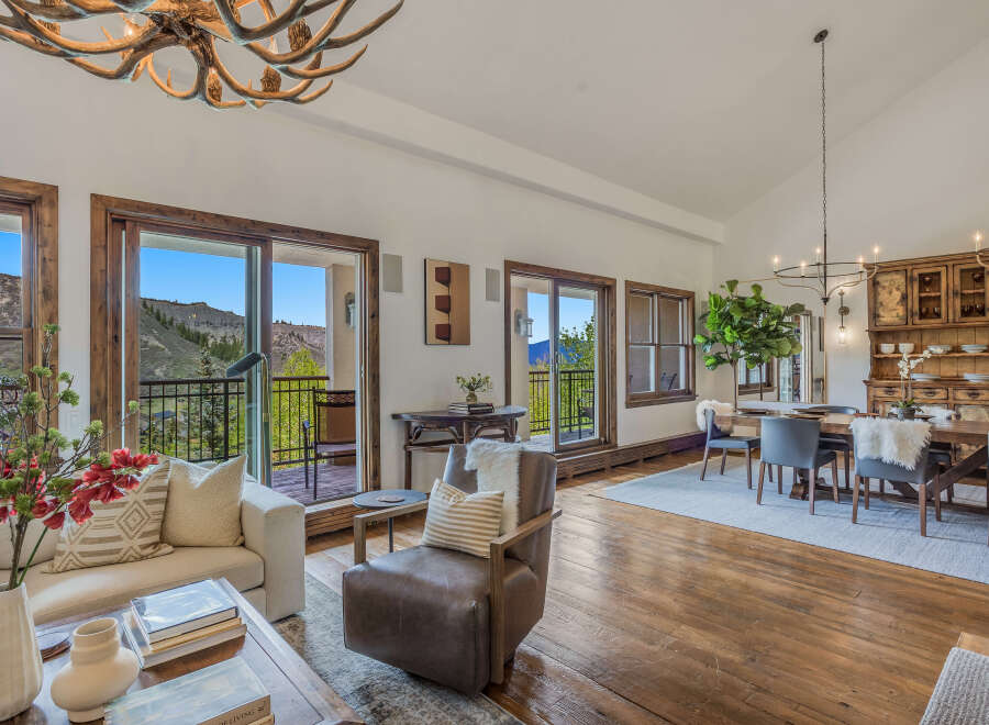 Experience luxurious mountain living in this stunning open-concept great room, featuring a rustic antler chandelier and expansive windows with breathtaking views.
