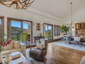 Experience luxurious mountain living in this stunning open-concept great room, featuring a rustic antler chandelier and expansive windows with breathtaking views.