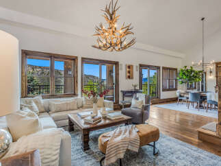 Experience luxurious mountain living in this stunning living and dining area, featuring a grand antler chandelier and expansive windows with breathtaking views.