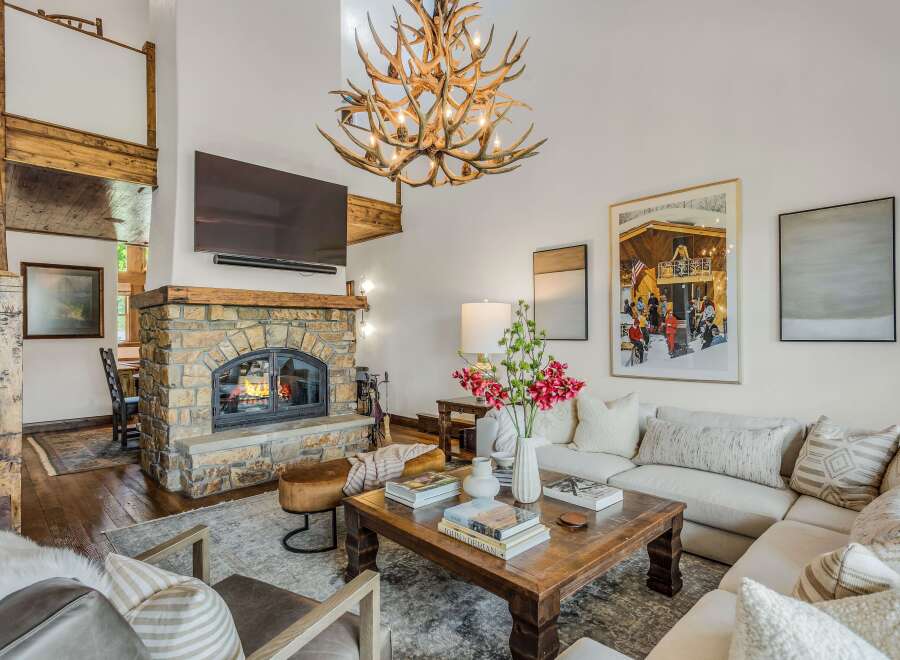 Experience rustic luxury in this stunning living room, featuring a grand stone fireplace and a unique antler chandelier.