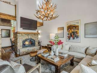 Experience rustic luxury in this stunning living room, featuring a grand stone fireplace and a unique antler chandelier.