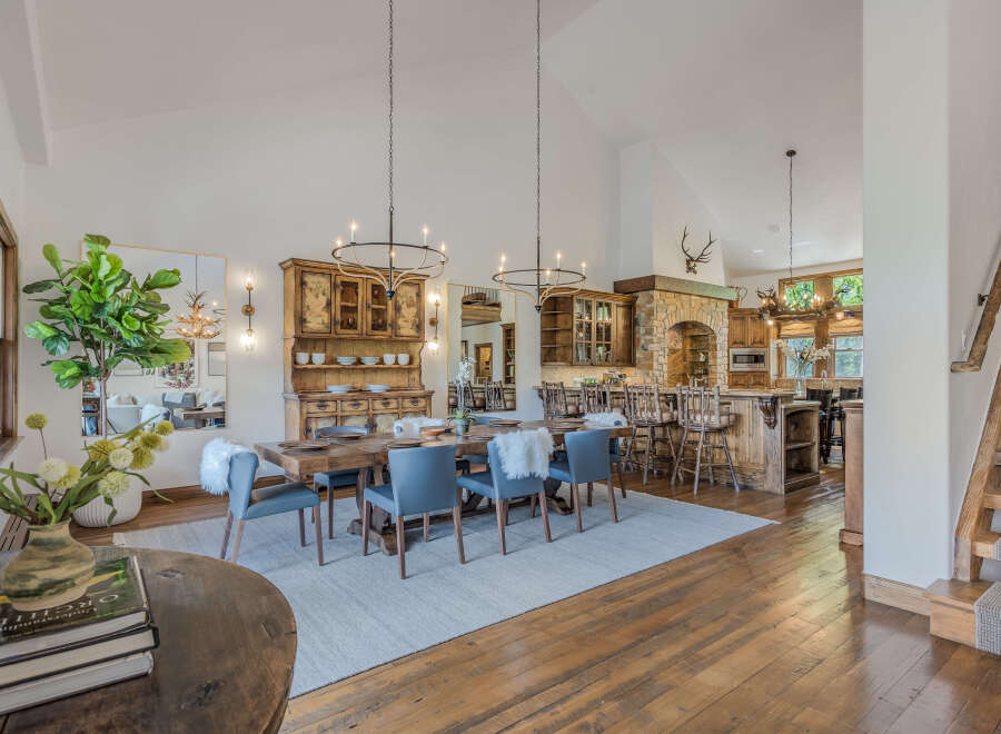 Experience rustic elegance in this spacious dining and kitchen area, featuring a large wooden dining table with plush seating, complemented by a charming hutch and a stone fireplace.