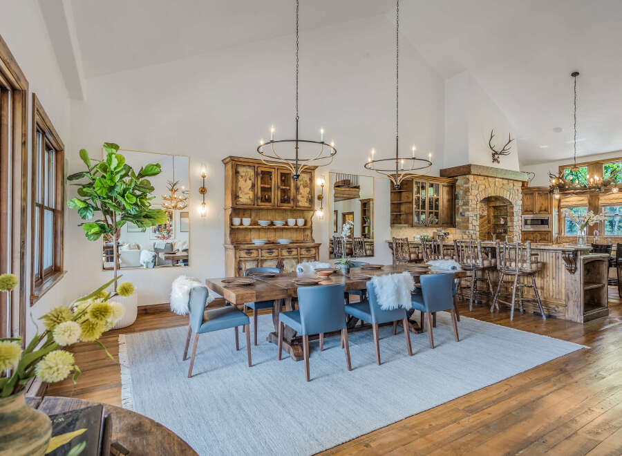 Experience rustic elegance in this spacious dining and kitchen area, featuring a large wooden dining table with comfortable blue chairs and a cozy rug.