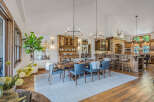 Experience rustic elegance in this spacious dining and kitchen area, featuring a large wooden dining table with comfortable blue chairs and a cozy rug.