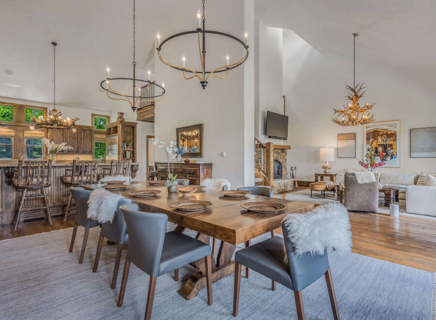 Experience rustic elegance in this spacious dining area, featuring a grand wooden table set for intimate gatherings and a stunning antler chandelier overhead.