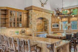 Experience rustic elegance in this stunning kitchen, featuring a grand stone fireplace with a mounted deer head and a unique antler chandelier.