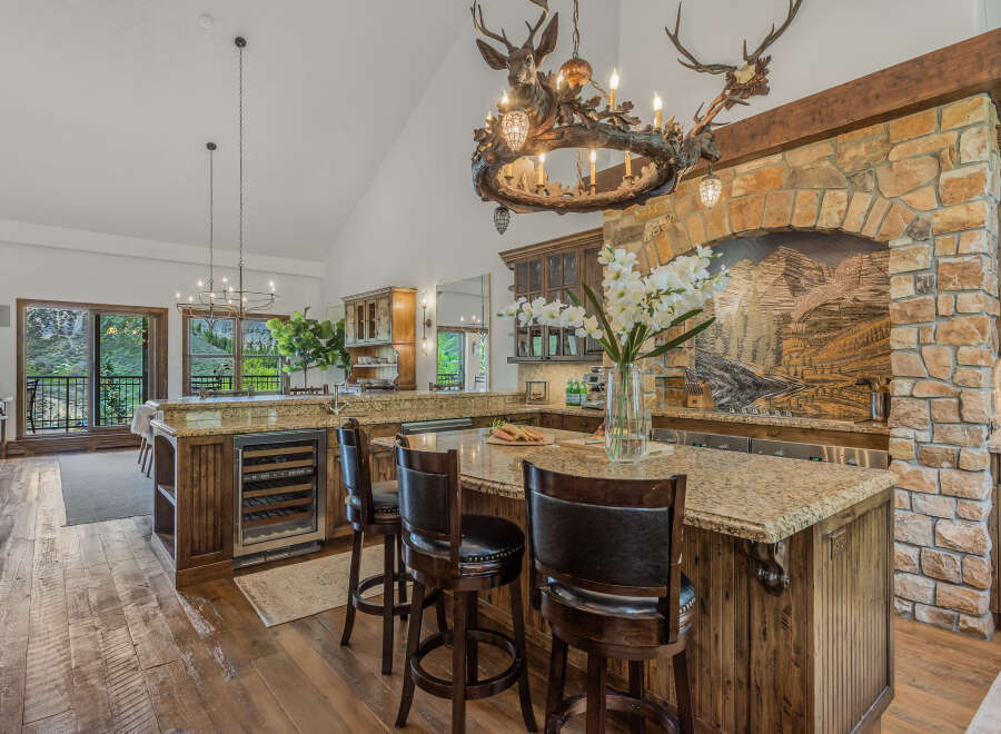Experience rustic luxury in this stunning mountain kitchen, featuring a grand stone fireplace and a unique antler chandelier.