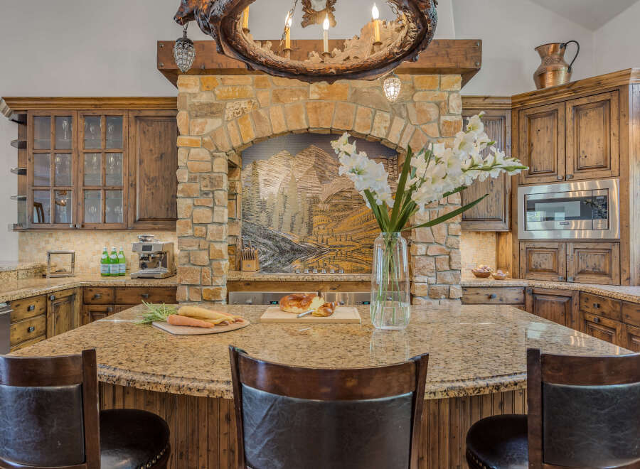 Experience luxury in this stunning kitchen featuring custom wood cabinetry and a grand stone fireplace with an intricate mosaic backsplash.