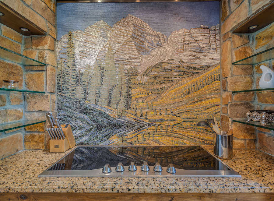 This stunning kitchen features a unique mosaic backsplash depicting a mountain landscape, adding a touch of artistry to the space.