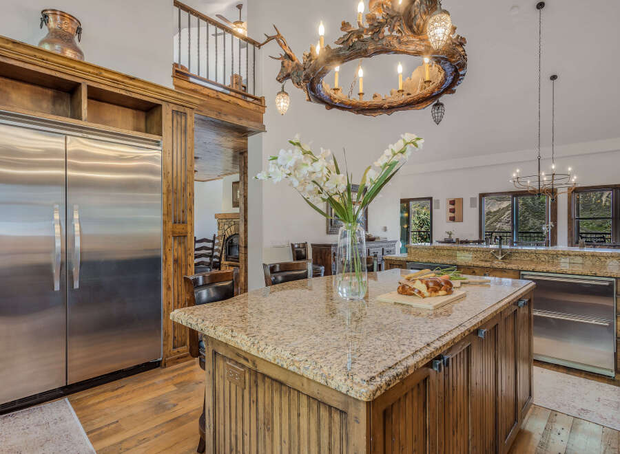 Experience rustic luxury in this stunning kitchen featuring a large granite island with a cutting board and fresh bread, perfect for entertaining.