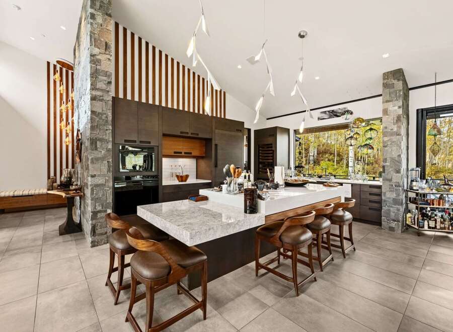 Experience luxury living in this stunning modern kitchen, featuring a large waterfall island with ample seating and a sleek, dark wood cabinetry.