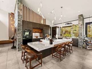Experience luxury living in this stunning modern kitchen, featuring a large waterfall island with ample seating and a sleek, dark wood cabinetry.