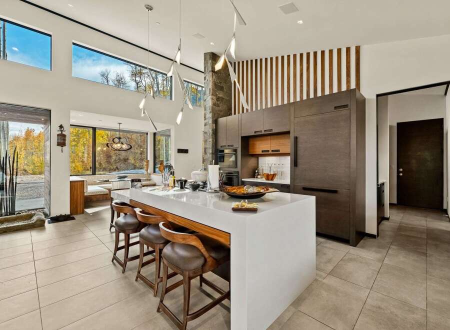 Experience modern luxury in this stunning open-concept kitchen, featuring a sleek white island with waterfall edges and comfortable leather bar stools.