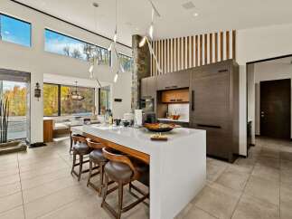 Experience modern luxury in this stunning open-concept kitchen, featuring a sleek white island with waterfall edges and comfortable leather bar stools.