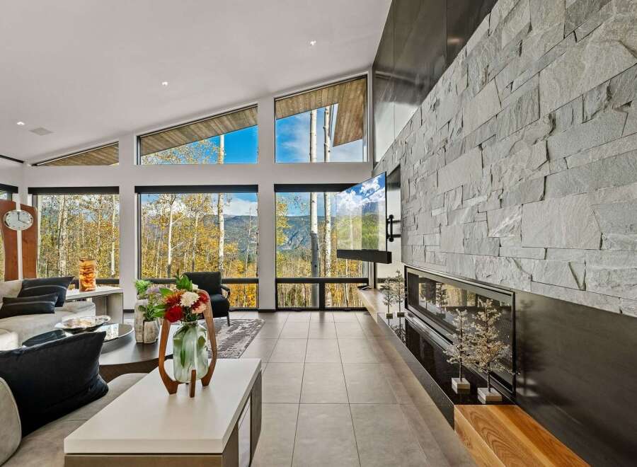 Experience breathtaking mountain views from this stunning living room, featuring a dramatic floor-to-ceiling stone fireplace and a large, wall-mounted television.