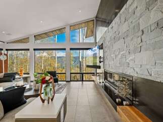 Experience breathtaking mountain views from this stunning living room, featuring a dramatic floor-to-ceiling stone fireplace and a large, wall-mounted television.