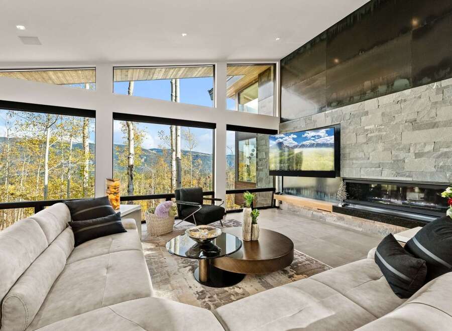 Experience breathtaking mountain views from this modern living room, featuring expansive windows that frame the vibrant autumn foliage.