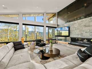 Experience breathtaking mountain views from this modern living room, featuring expansive windows that frame the vibrant autumn foliage.