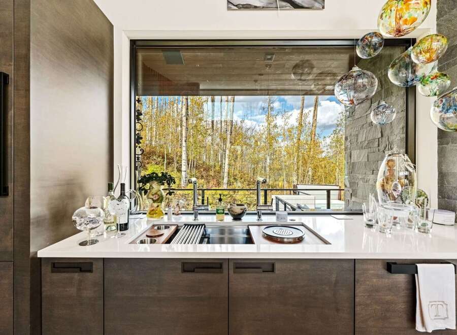Experience luxury living with this stunning kitchen featuring a large sink area overlooking a breathtaking forest view.