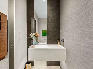 Discover modern elegance in this powder room, featuring a sleek floating vanity and a striking dark tiled accent wall.