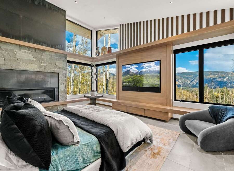 Experience luxury mountain living in this stunning bedroom featuring a modern stone fireplace and a large flat-screen TV.