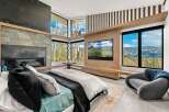 Experience luxury mountain living in this stunning bedroom featuring a modern stone fireplace and a large flat-screen TV.